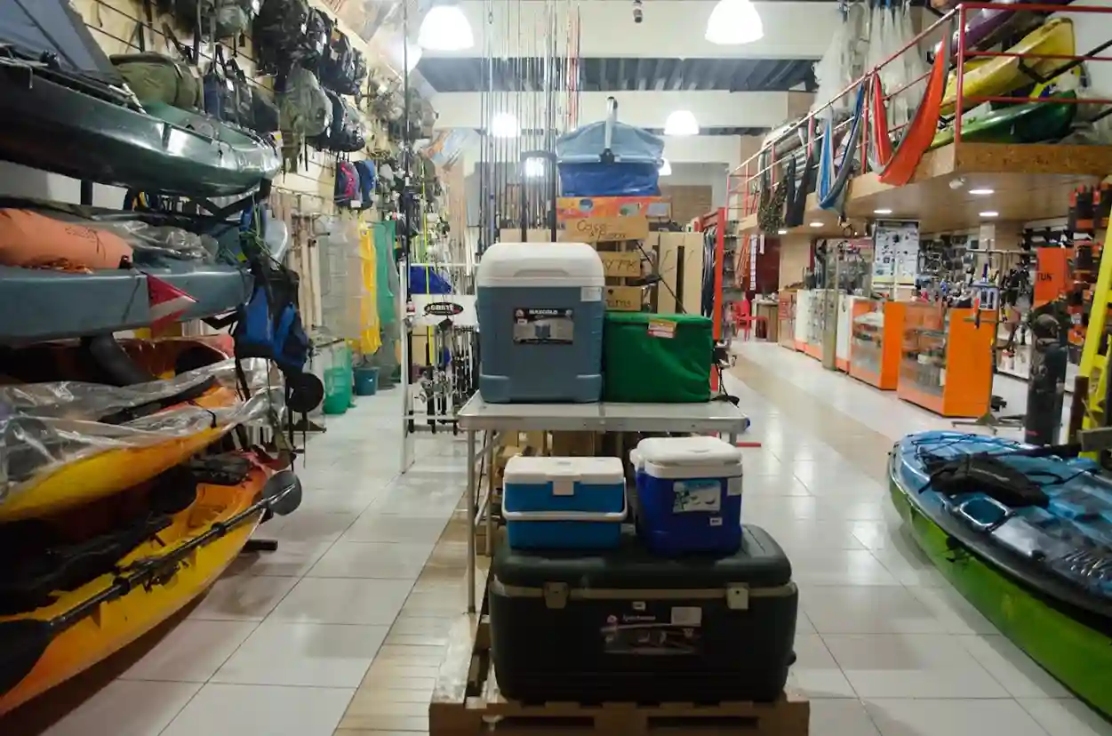 Corredor da loja com caiaques, caixas térmicas e varas de pesca